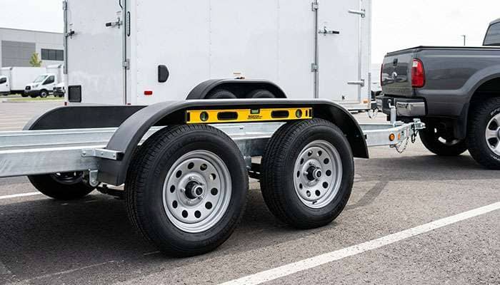 Tandem axle trailer hitched to a pickup with a level resting on the trailer frame rail to check that the axles share load evenly
