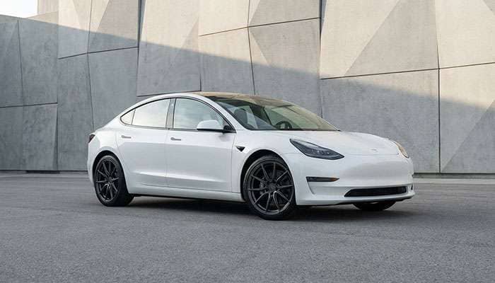 White Tesla Model 3 with black aftermarket wheels parked in front of a modern building wall