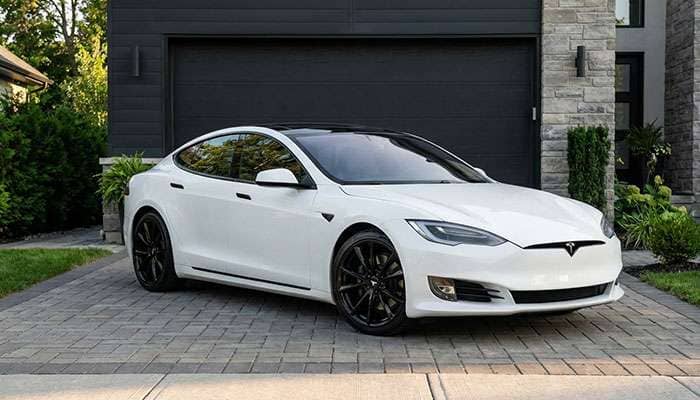 White Tesla Model S with black T Sportline wheels parked in front of a dark garage door