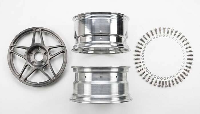 Three-piece forged wheel disassembled showing forged center, inner barrel half, outer barrel half, and assembly hardware