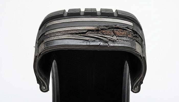 Cutaway view of a failed tire showing separated steel belts and degraded rubber from heat damage