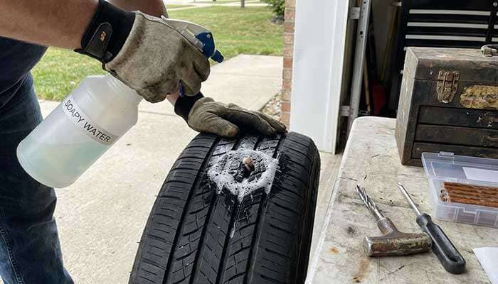 Person holding a spray bottle and preparing to repair a flat tire using a tire plug kit