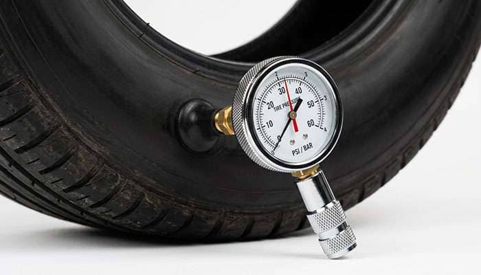 Dial tire pressure gauge pressed onto a tire valve stem taking a cold inflation reading