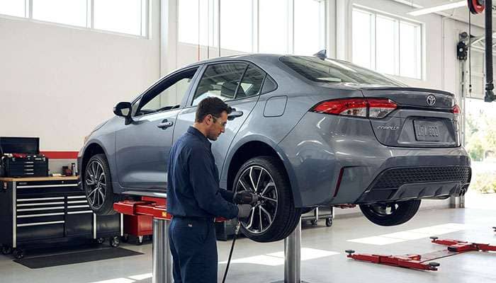 Technician wearing gloves rotating a tire on a vehicle lifted in an auto service garage