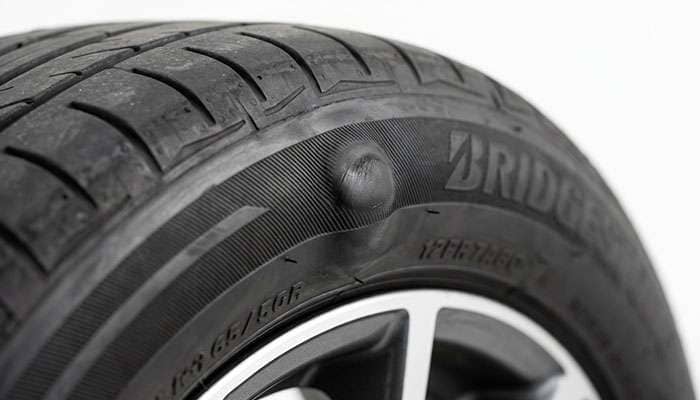Close-up of a bulge in the sidewall of a passenger car tire indicating internal cord damage