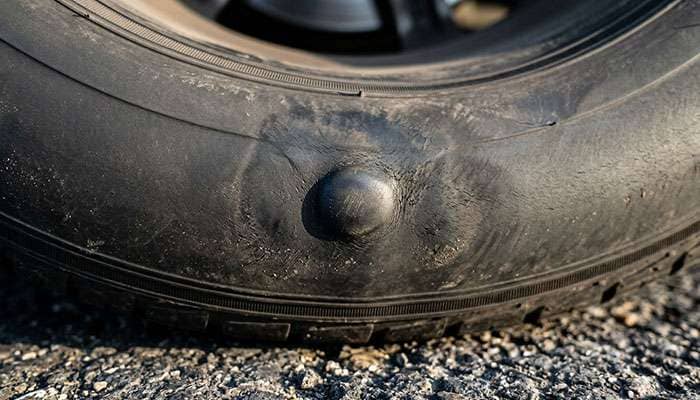 Close-up of a tire sidewall showing impact bruising and a small bulge from pothole pinch damage