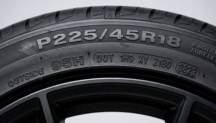 Close-up of a tire sidewall showing the speed rating letter alongside the load index number and DOT date code stamping