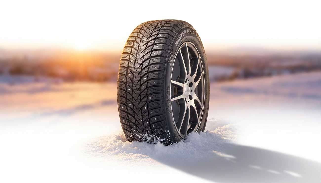 Close-up of a car tire with winter siping driving through snow at sunset for better winter grip