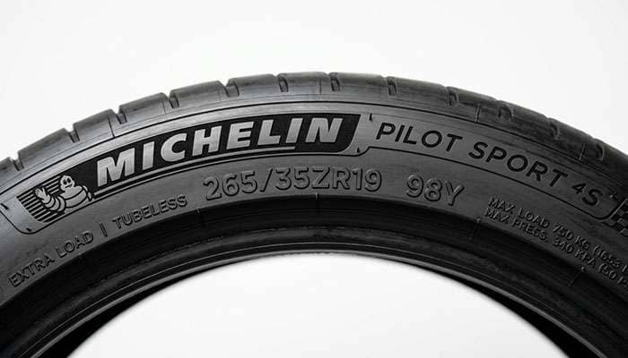 Tire sidewall close-up showing size, load index, and speed rating markings on a clean white seamless studio backdrop