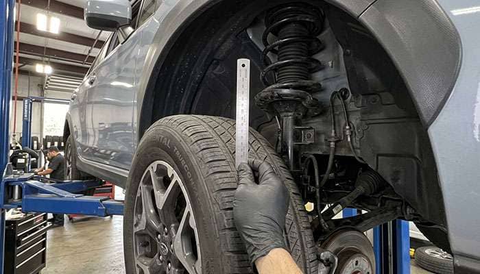 Technician measuring the gap between the inner sidewall of a crossover tire and the front strut with a ruler
