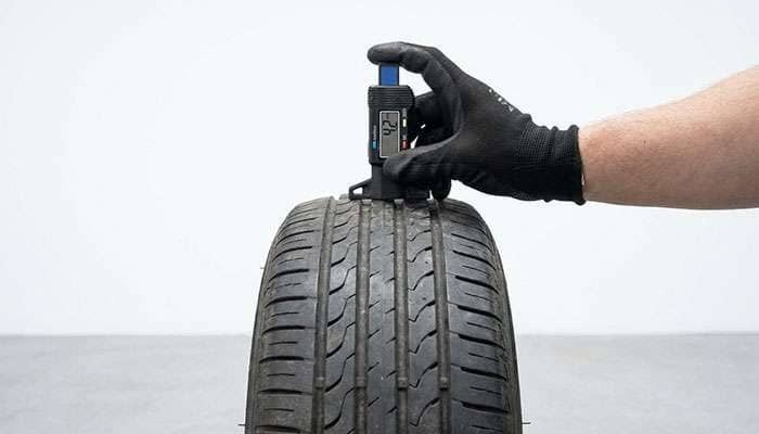 Hand using a tire tread depth gage to measure the tread on a car tire for safety inspection
