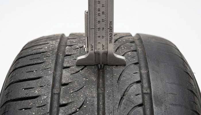 Tread depth gauge inserted into a tire groove showing a worn reading close to the two thirty-seconds limit