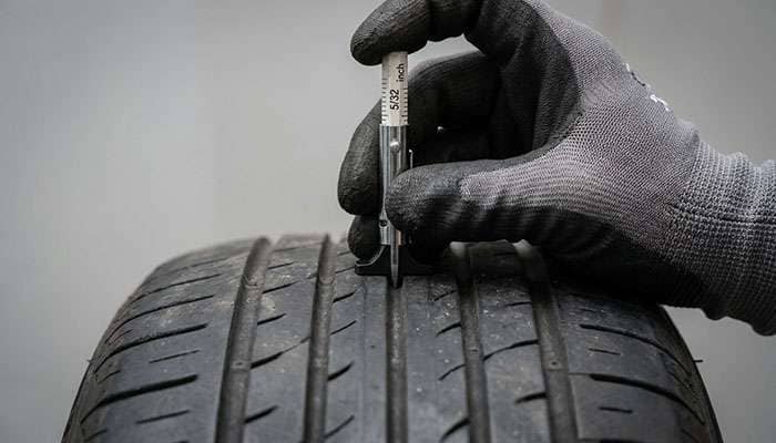 Hand using a tread depth gage to measure the tread depth of a car tire
