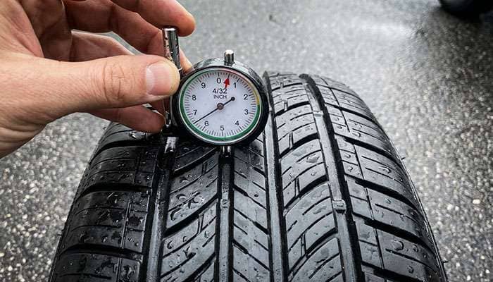 Measuring tire tread depth with gauge showing minimum safe depth for rain driving