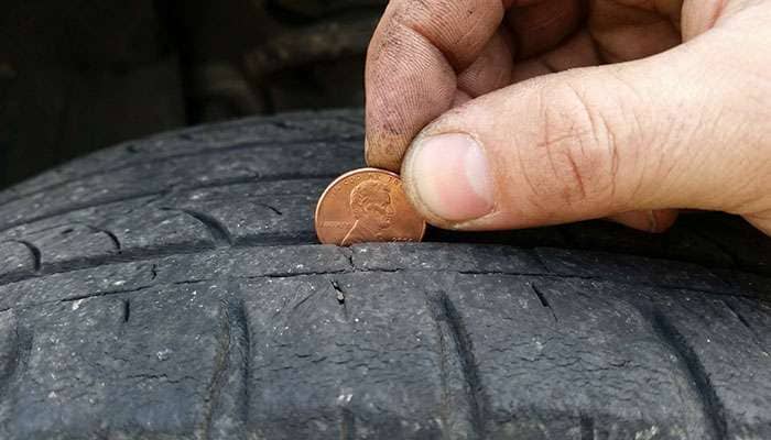 Hand holding a penny against a worn tire tread showing minimal depth