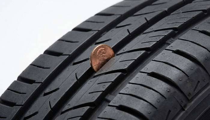 Close-up of a tire tread with the text Properly Check Tread Wear emphasizing tire maintenance for Tesla Model 3 or Y
