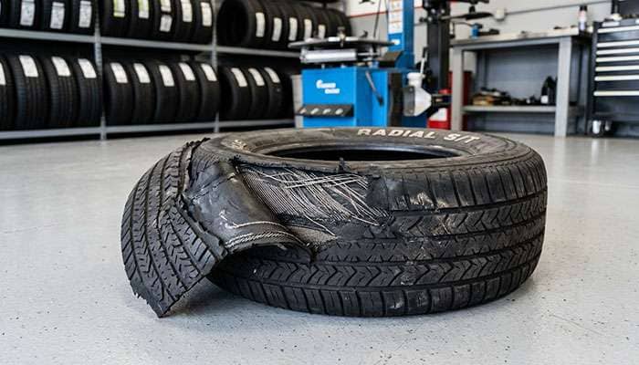 Passenger tire with tread separation from heat and overload damage lying on a tire shop floor