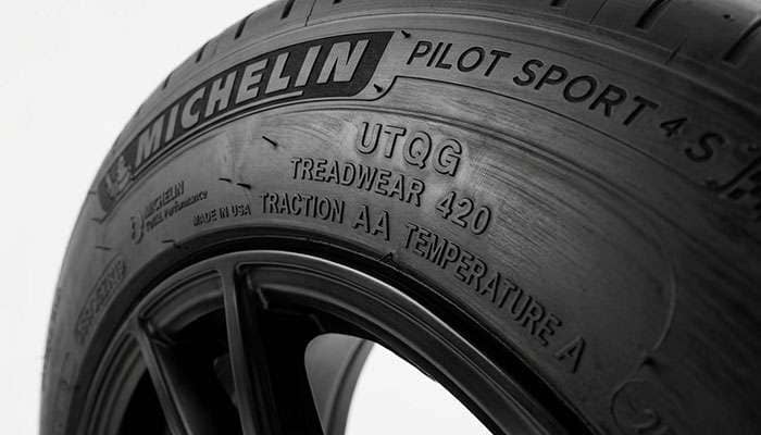 Tire sidewall close-up highlighting the UTQG treadwear, traction, and temperature markings against a clean white studio backdrop