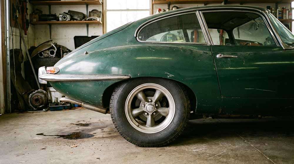 Close-up of a green classic car's rear side showcasing a Torq Thrust mag wheel in a garage setting