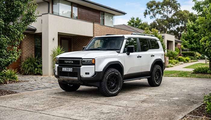 Side view of a 2024 Land Cruiser 250 with large off-road tires and black rims parked in a residential driveway.