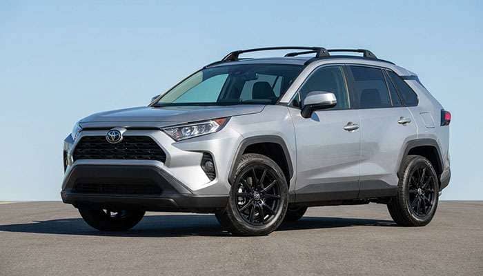 Silver Toyota RAV4 with black aftermarket wheels and roof rack parked on asphalt under a blue sky.
