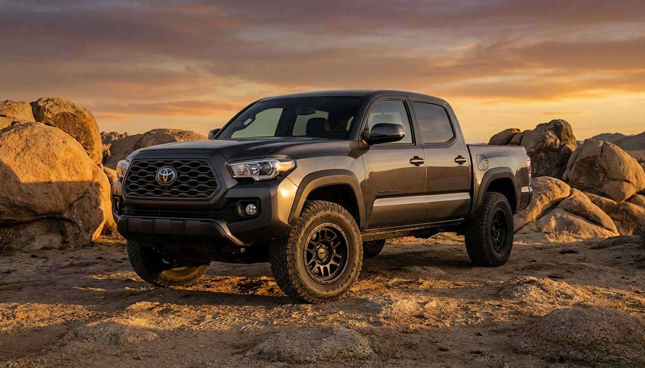 Toyota Tacoma pickup truck with aftermarket black wheels parked on rocky terrain at sunset
