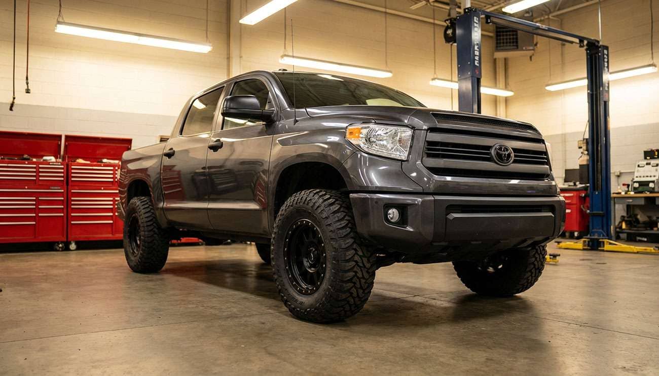 Toyota Tundra truck with aftermarket off-road tires in a garage workshop setting with tools in the background