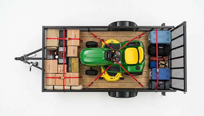 Utility trailer with properly loaded cargo showing heavy items positioned over and forward of the axle with tie-down straps on a clean white surface