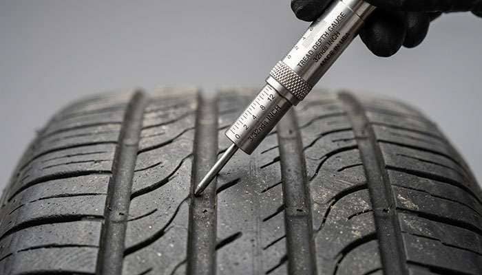 Close-up of a tread depth gauge being inserted into the groove of a tire to measure remaining tread in 32nds of an inch