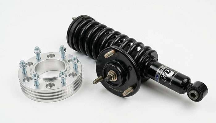 Aluminum strut spacer leveling kit shown next to a coilover strut assembly from a full-size pickup truck front suspension