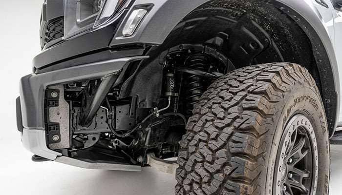 Inside the front wheel well of a pickup truck showing the plastic fender liner, mud flap mounting area, and the crash bar structure behind the tire