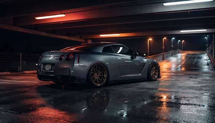 Gray sports car with bronze deep-dish wheels and aggressive lowered fitment in parking garage at night