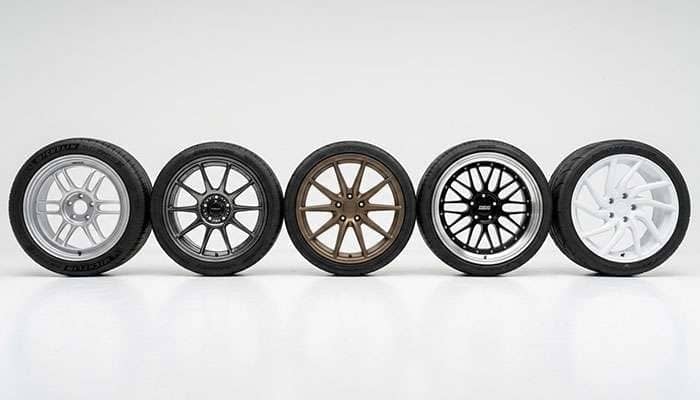 Five tuner wheels from different brands in various finishes and spoke designs on a clean white studio surface