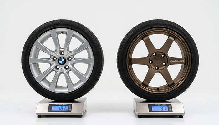 Lightweight tuner wheel on a scale next to a heavier stock wheel showing the weight difference on a clean white surface