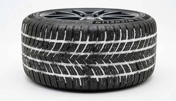 Close-up of an ultra-high-performance all-season tire showing tread blocks with light snow accumulation indicating cold-weather grip
