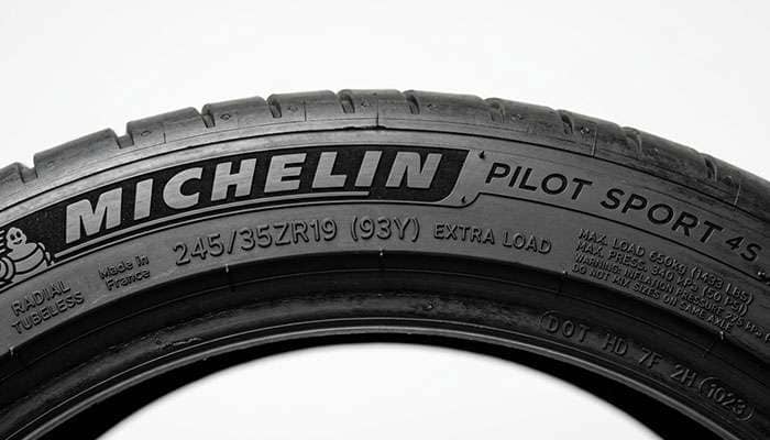 Close-up of a tire sidewall showing UTQG treadwear, traction, and temperature rating codes on a clean white seamless studio backdrop