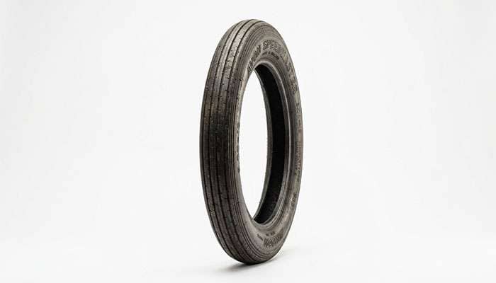 A vintage clincher-style motorcycle tire with smooth tread against a clean white studio backdrop