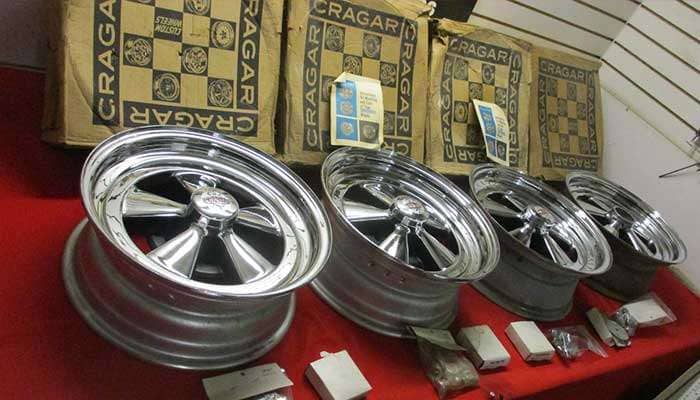 Four vintage Cragar GT SS 15x6 chrome wheels displayed on a red surface with original boxes behind them
