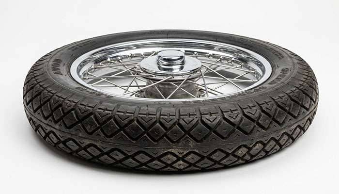 Close-up of a vintage motorcycle tire's diamond tread pattern against a clean white studio backdrop