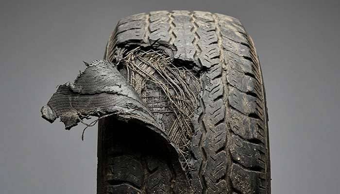 Close-up view of a vintage tire showing tread separation damage where the outer tread layer has partially pulled away from the belt package due to excessive sustained speed