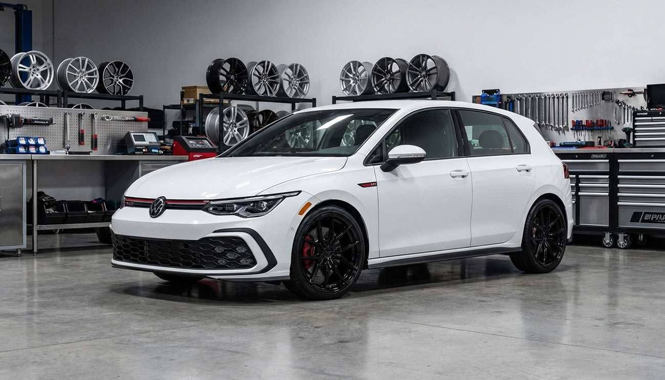 White Volkswagen GTI with black aftermarket wheels in a garage surrounded by wheel rims and tools