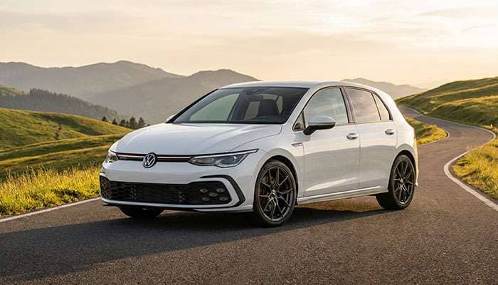 White Volkswagen Golf GTI with custom wheels parked on a mountain road with scenic hills in the background