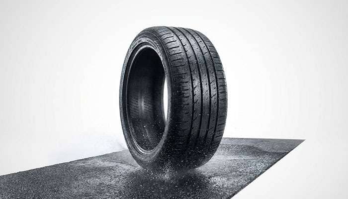 Close-up of car tire on wet road surface with water spray demonstrating wet weather testing conditions