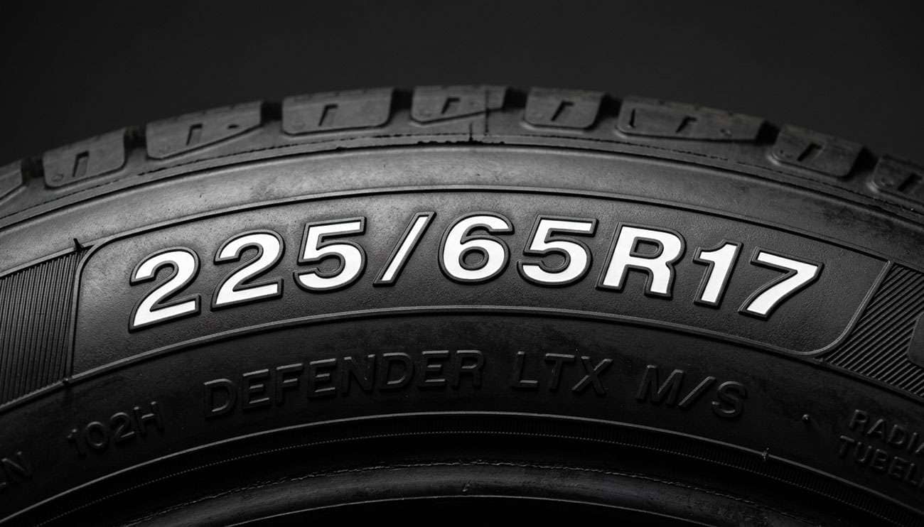 close-up of a tire sidewall showing the full tire size number code with labels pointing to width aspect ratio and rim diameter