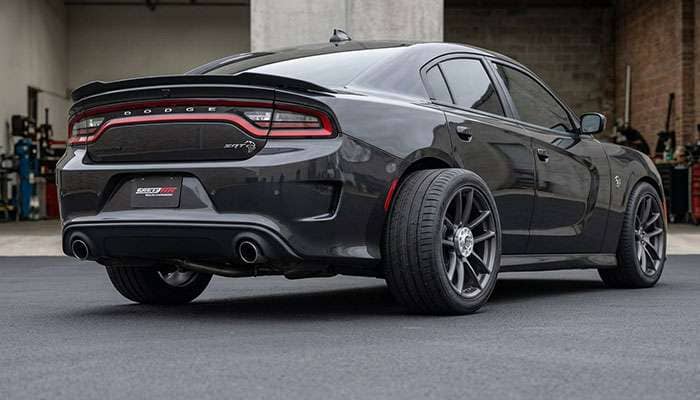 Rear view of a muscle sedan showing one tire tucked under the fender and the other pushed out past the fender on a thick wheel adapter