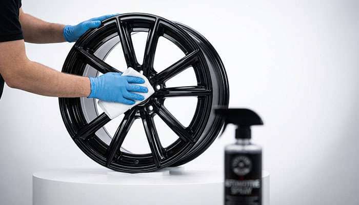 Person cleaning a shiny black car wheel with a white microfiber cloth outdoors