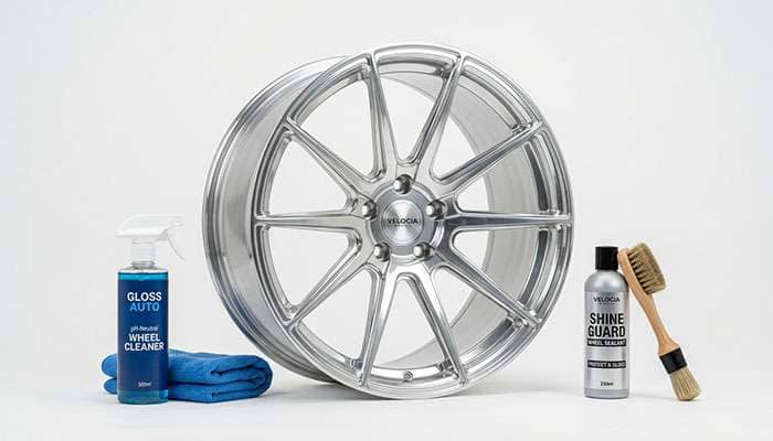 Clean aluminum wheel arranged with detailing supplies including microfiber towel ceramic coating and wheel sealant on a clean white studio backdrop