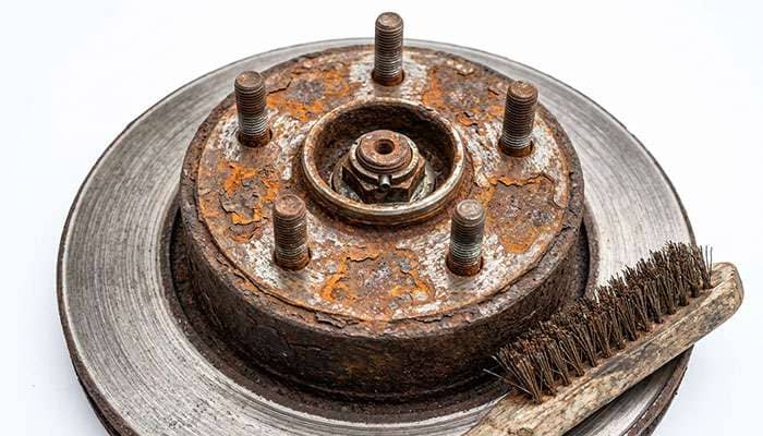 vehicle hub face with flaking rust and scale on the wheel mounting surface next to a wire brush used for cleaning