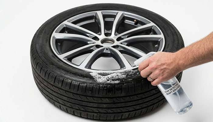 hand spraying soapy water solution along the tire tread and rim edge of a mounted wheel to locate a slow air leak