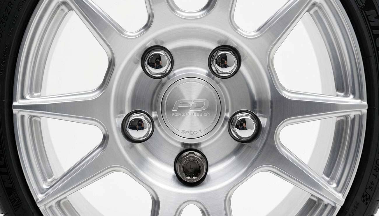 Close-up of a locking lug nut installed on a custom wheel next to a standard lug nut showing the security pattern difference